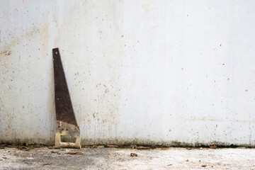 The rusty old hand saw leaning against a white wall background