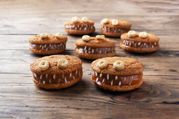 Cookies with cream paste in the shape of monsters for Halloween celebration. Funny homemade faces made of oatmeal cookies and boiled condensed milk.