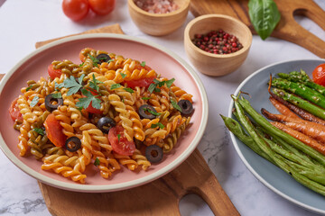 Three Colors Rotini Pasta.  Abstract texture of colorful pasta. Pattern of macaroni. Tasty appetizing classic italian spaghetti pasta with tomato sauce, cheese and basil on plate.