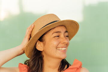Latin girl with freckles on her face smiling and holding her hat looking to the side
