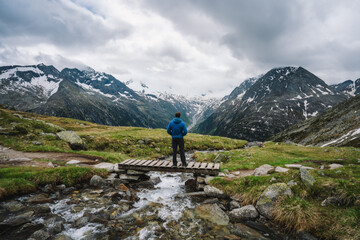 Man hiker resting on small bridge over mountaian river at Schlegeis Lake, Zillertal Alps, Austria