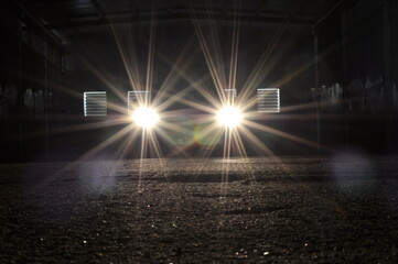 The car is standing in the dark in the garage and lights are on to illuminate the road under the car