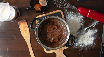 dough for delicious brownie cake on dark wooden table next to ingredients and cooking utensils, top view.
