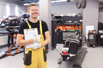 Young male locksmith in uniform stands in workshop and holds clipboard with documents in hands