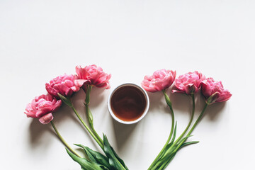 A beautiful cup of coffee or black tea on a white background decorated with pink tulips. Flat lay, top view.