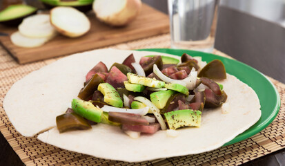 salad of black tomatoes, avocado and onions in Italian tortilla on green plate
