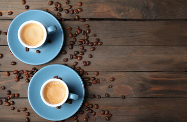 Cups of tasty espresso and scattered coffee beans on wooden table, flat lay. Space for text