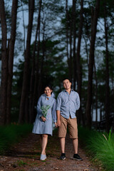 Portrait Pre Wedding of an Asian couple dressed in the same blue tones posing in a pine garden expressing their love in happiness behind an out-focused pine tree.