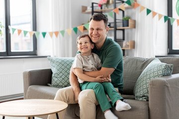 Obraz premium family, fatherhood and people concept - portrait of happy smiling father and little son sitting on sofa at home party
