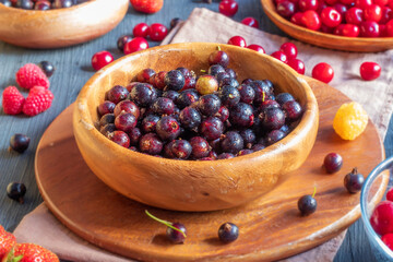 In a wooden shallow bowl there is a ripe black currant with drops of water