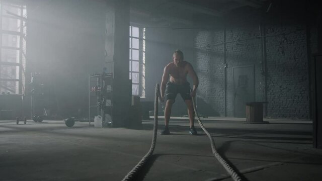 Man practicing exercise with battle ropes. Sportsman doing functional training