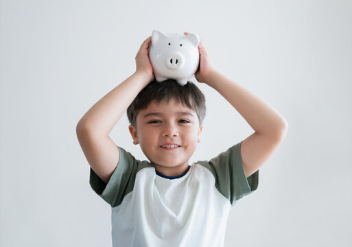Happy boy putting piggy bank on his head on white background.isolated child with smiling face showing money saving box.kid Learning financial responsibility and planning about saving money for future