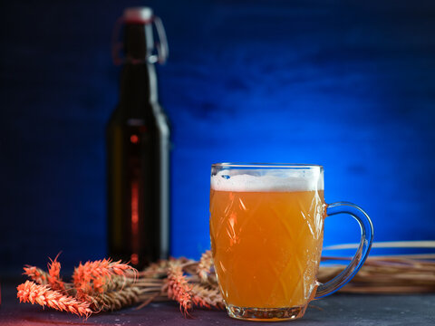 A mug of cold unfiltered wheat beer on a dark background with a blue backlight. Bugel bottle