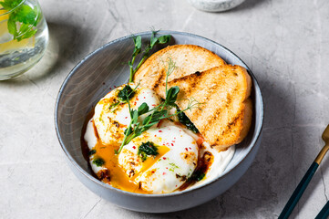 Cilbir or Turkish Eggs. dish served as mezze: poached eggs topped over herbed greek yogurt, then drizzled with hot spiced paprika olive oil. Turkish breakfast in a grey bowl on marble background