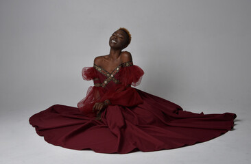 Full length portrait of pretty African woman wearing long red renaissance medieval fantasy gown,...