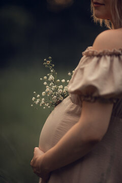 a pregnant woman in a beige dress holds a hand on a tummy. Waiting for a baby, pregnant photo session. pregnancy and childbirth in the summer, 9 months. motherhood concept