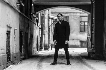 Long-haired guy stands in a snow-covered arch in a black coat