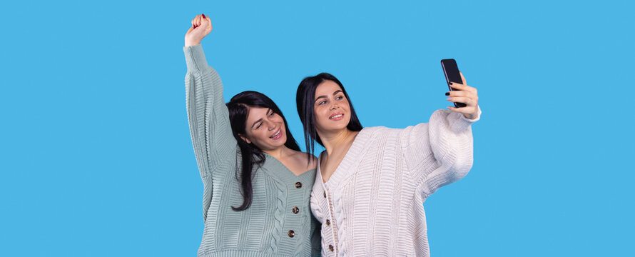 Cheerful twin girls making selfie isolated on blue background one of them raised her right hand up and smiling. - Powered by Adobe