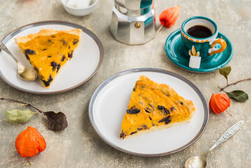 Sliced open pie with pumpkin and prunes on a ceramic plate on a gray concrete background. Pumpkin recipes. Thanksgiving desserts.