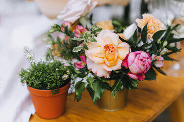 Multicolored flowers, roses, wild flowers in pots close-up stand on a wooden table.