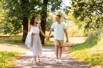 Fototapeta premium leisure, vacation and people concept - happy couple with picnic basket and blanket walking at summer park