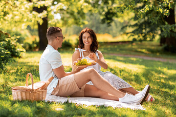 leisure and people concept - happy couple with food having picnic at summer park
