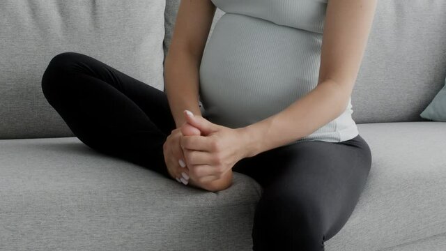 Pregnant woman massaging her swollen foot while sitting on couch at home