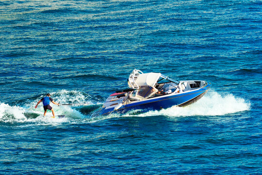 Summer water sports, wakeboarding. Young man riding wakeboard on wave of motorboat