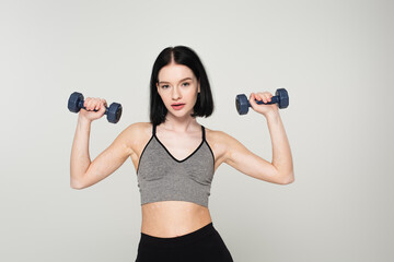 Sportswoman with vitiligo training with dumbbells isolated on grey