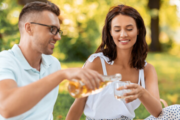 leisure and people concept - happy couple having picnic and pouring wine to glass at summer park