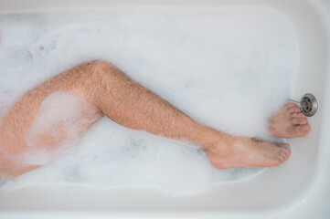 Fototapeta premium Funny picture of a man taking a relaxing bath. Close-up of male feet in a bubble bath. Top view