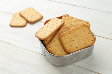 Cracker cookies in a stainless steel bowl on white wooden table background.