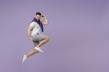 Full size body length strong sporty fitness young brunet man 20s wear white t-shirt purple shirt jump show biceps muscles on hand strength power isolated on pastel violet background studio portrait