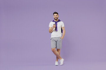 Fototapeta na wymiar Full size body length happy cheery young brunet man 20s wear white t-shirt purple shirt hold takeaway delivery craft paper brown cup coffee to go isolated on pastel violet background studio portrait