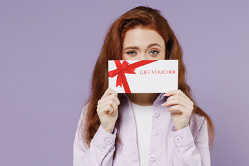Happy young redhead curly woman 20s wears white T-shirt violet jacket hold hide behind gift certificate coupon voucher card for store isolated on pastel purple color wall background studio portrait - obrazy, fototapety, plakaty