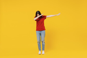 Fototapeta na wymiar Full size body length fascinating young brunette woman 20s wears basic red t-shirt doing dab hip hop dance hands move gesture youth sign hide cover face isolated on yellow background studio portrait