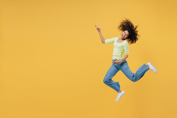 Fototapeta na wymiar Full size body length happy african american young woman 20s wears green shirt jump do guitar gesture keep eyes closed isolated on yellow background studio portrait. People emotions lifestyle concept