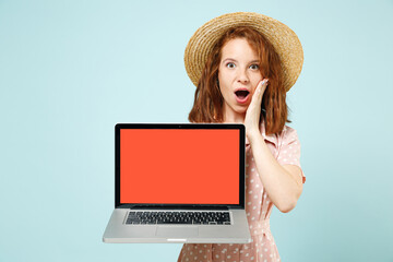 Smiling happy young redhead curly woman 20s hold in hand laptop pc computer with blank screen workspace area wears casual pink dress straw hat isolated on pastel blue color background studio portrait.