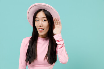 Curious nosy fun young brunette asian woman 20s wears pink clothes hat try to hear you overhear listening intently isolated on pastel blue color background studio portrait. People emotions concept