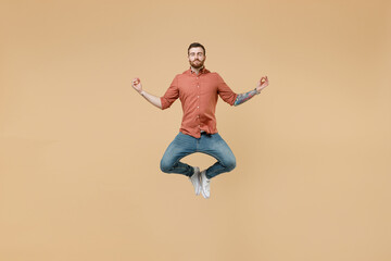 Fototapeta na wymiar Full size body length tatooed young brunet man 20s short haircut wears apricot shirt jump hold spread hands in yoga om aum gesture relax meditate isolated on pastel orange background studio portrait.