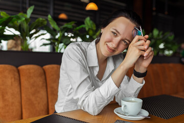 Delighted businesswoman having coffee break in restaurant while sitting at table and looking at camera 