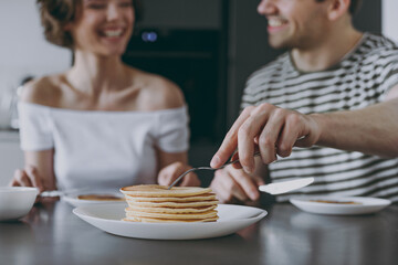 Close up young couple two woman man in casual t-shirt clothes sit by table eat pancakes have breakfast cook food in light kitchen at home together People lifestyle concept. Focus on fork griddle-cake.