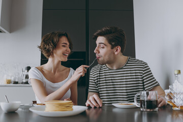 Young happy couple two woman man 20s in casual t-shirt clothes sit by table eat pancakes with maple...