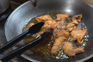 Cooking deep fried chicken on a steel wok at the kitchen. Frying with vegetable oil. Closeup shot.