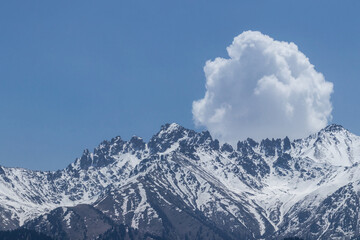A view of the snowy peaks of the mountains, and behind them a white rounded cloud
