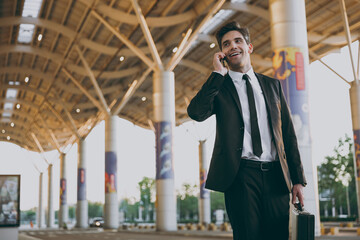 Bottom view traveler businessman man in black dinner suit stand outside at international airport terminal with attache case talk on mobile phone book taxi order hotel Air flight business trip concept.