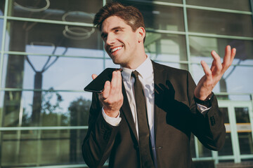 Fototapeta premium Bottom view friendly traveler businessman young man in black suit stand outside at international airport terminal use mobile phone book taxi order hotel record voice Air flight business trip concept.
