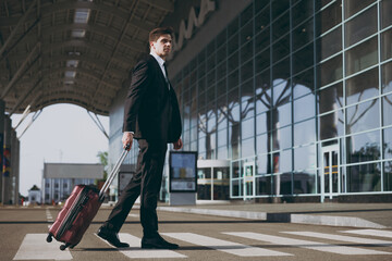 Side bottom view full size minded young traveler businessman man in black suit walk go outside at international airport terminal with suitcase valise crossing road Air flight business trip concept.