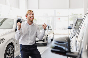 Naklejka na ściany i meble Man excited customer buyer businessman client in white shirt choose auto do winner gesture want buy new automobile in car showroom vehicle salon dealership store motor show indoor Car sales concept.