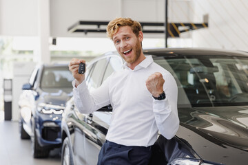 Fototapeta na wymiar Man winner happy customer buyer client in white shirt hold keys fob clench fist chooses auto want buy new automobile in car showroom vehicle salon dealership store motor show indoor. Sales concept